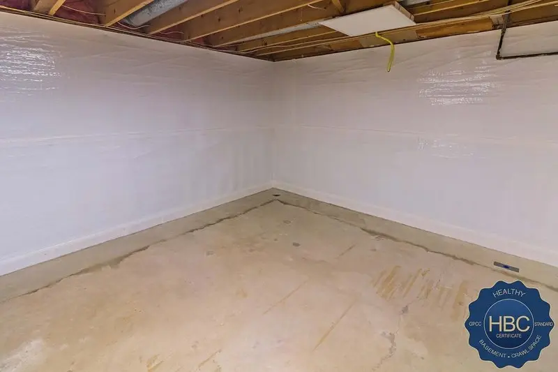 Empty basement corner with white painted walls and exposed wooden ceiling joists